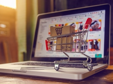 Laptop with toy shopping cart on keyboard to depict online shopping