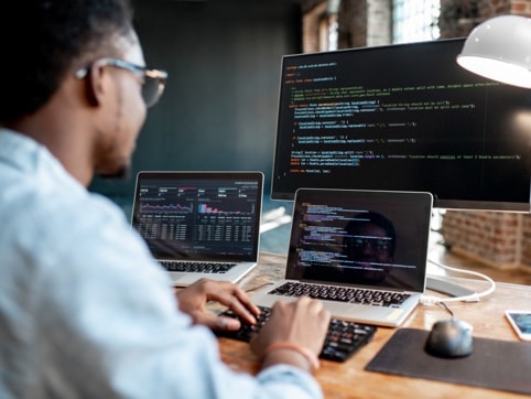 Man with two laptops and a screen with codes